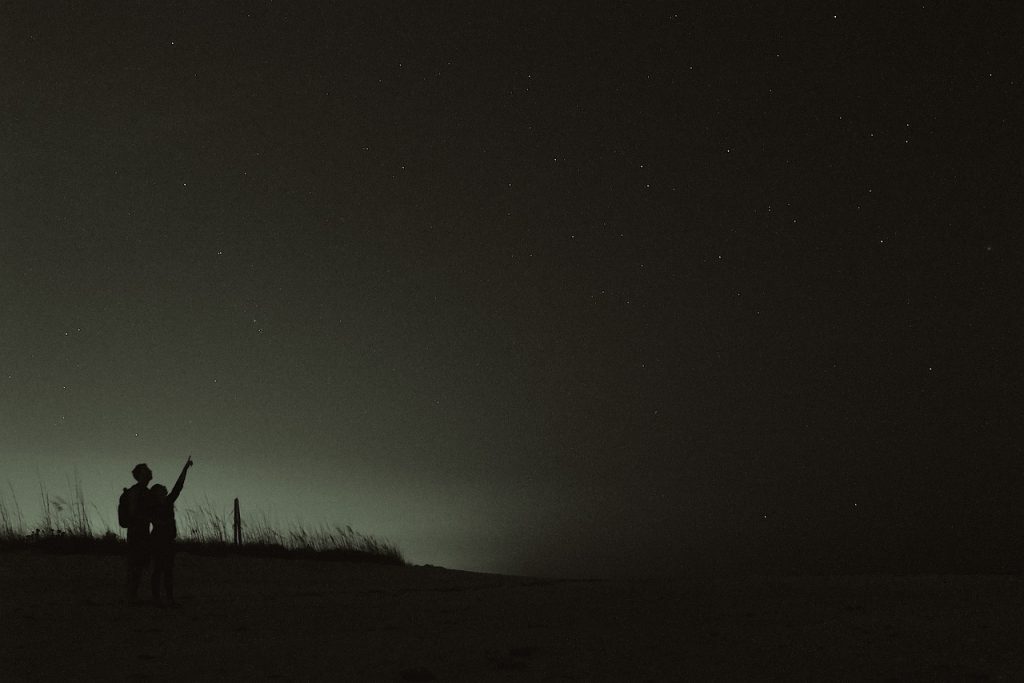 Two people watch a dark sky.