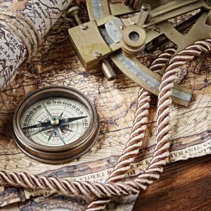 A collection of nautical items rest upon a desk: a sextant, map, rope and compass.